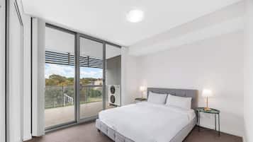 Une chambre d’hôtel moderne avec un grand lit, deux tables de chevet, une porte-fenêtre coulissante donnant sur un balcon et un luminaire au plafond.