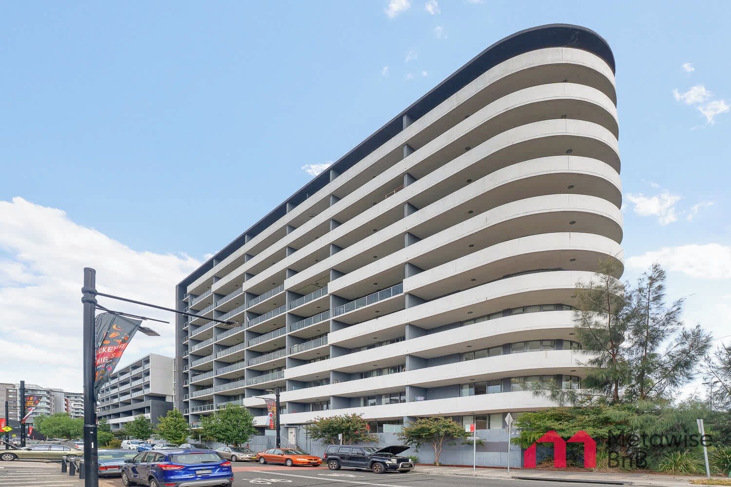 A multi-story hotel with a curved facade, balconies, and a parking lot in front.