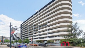 Ein mehrstöckiges Hotel mit geschwungener Fassade, Balkonen und einem Parkplatz davor.