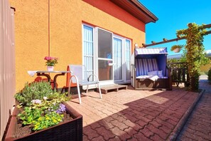 En uteplats med ett bord och stolar, en liten rabatt med blommor och en möblerad sittplats under tak.