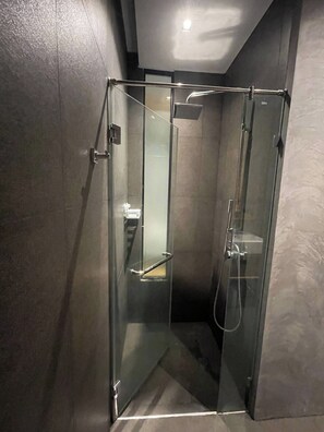 Un box de ducha con paredes de vidrio, con cabezal de ducha manual y espejo de mano.