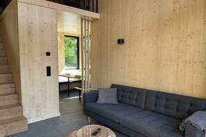 Ein Holzinnenraum mit einer Couch, einer Fernbedienung auf einem runden Tisch und einer Treppe.