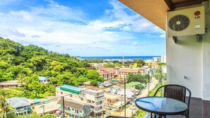 A balcony with a view of a coastal town, a table, and an air conditioning unit. - Sunset Sea-view Studio, Karon Beach 800 m, Pool, Fibre Wi-fi (Karon)