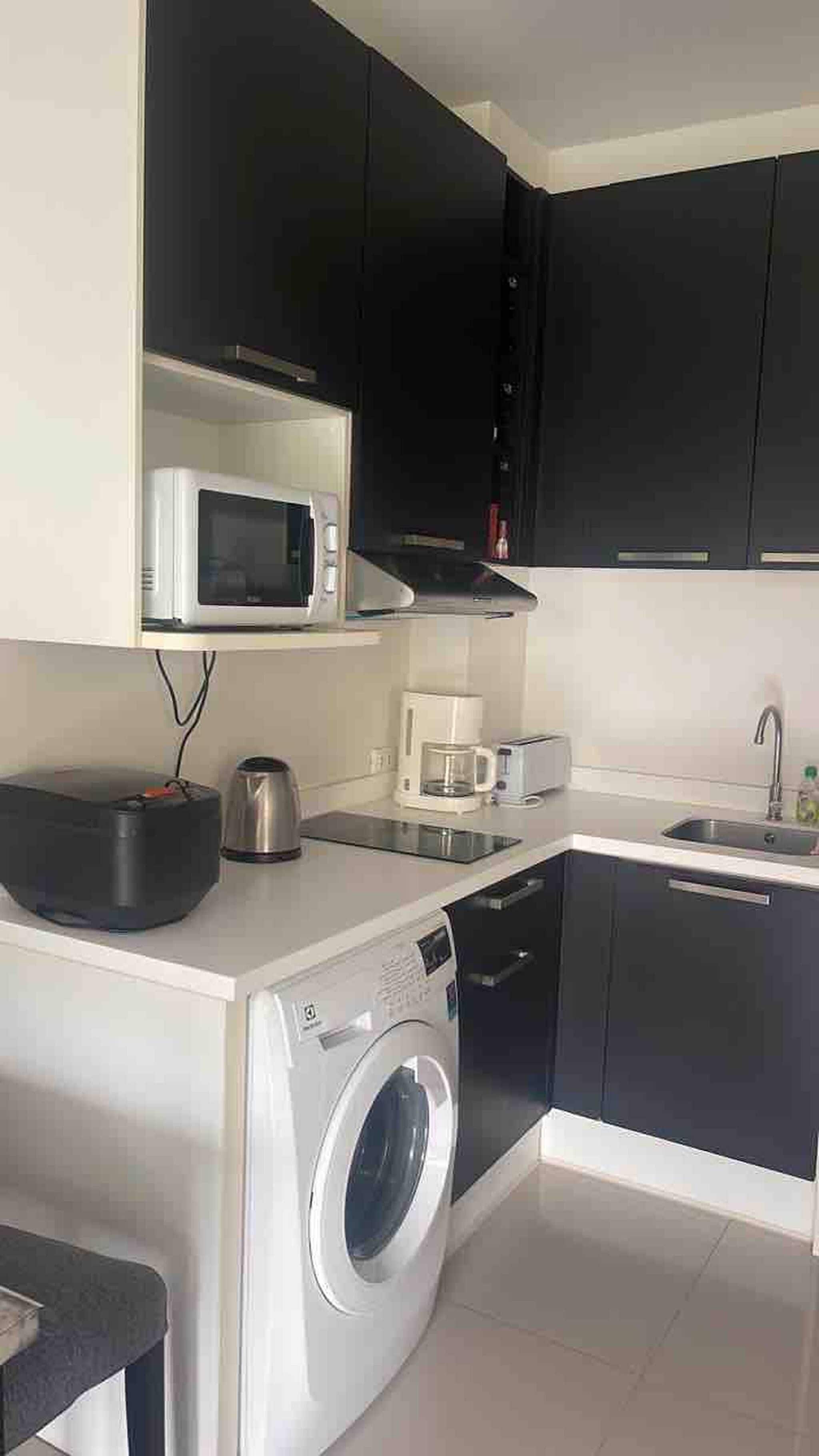 Una cocina compacta equipada con microondas, cafetera, tostadora y lavadora.