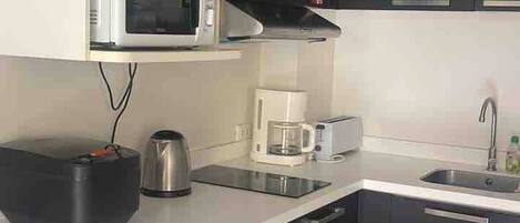 Una cocina compacta equipada con microondas, cafetera, tostadora y lavadora.