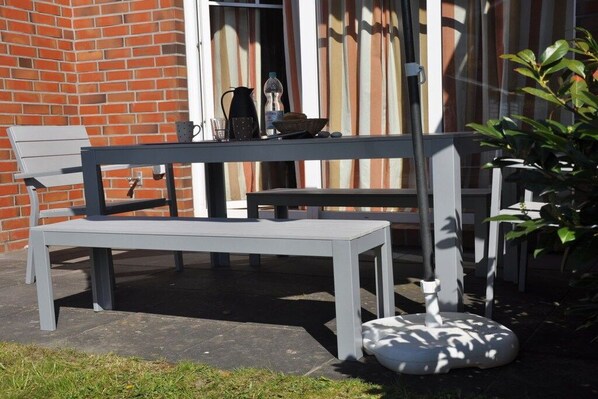 Un espace extérieur aménagé avec un banc et une table, un pot de fleurs et un mur de briques en arrière-plan.