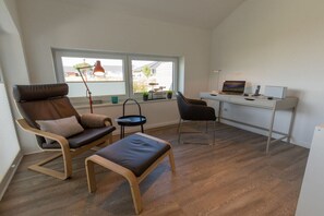 Una habitación con escritorio, dos sillas, una mesita, un banco y ventana con vistas.