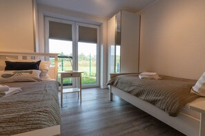 Ein Schlafzimmer mit zwei Betten, einem kleinen Tisch und Blick ins Freie durch eine Schiebetür.