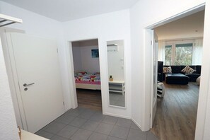 A room with a bed, a small table, and a mirror. There is a door leading to another room. - Holiday apartment with 2 bedrooms (Scharbeutz)