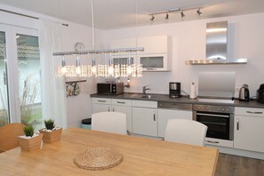 A modern kitchen with white cabinetry, stainless steel appliances, and a pendant light fixture. - Holiday apartment with 2 bedrooms (Scharbeutz)