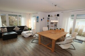 A modern living room with a sofa set, a dining table with chairs, and a bookshelf. - Holiday apartment with 2 bedrooms (Scharbeutz)
