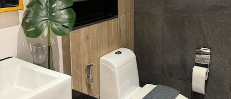 A modern bathroom with a white toilet, a sink, and a shower. There is a framed picture on the wall and a plant on the counter.