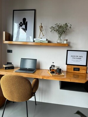 A workspace with a laptop, books, a wooden desk, a chair, and decorative items including a framed quote and a vase with flowers. - Top-floor Sea-view Studio, Nai Harn, Rooftop Pool (Rawai)