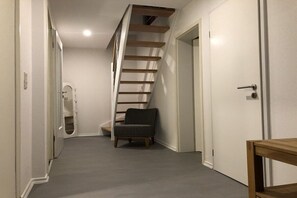 Ein schmaler Flur mit einer Treppe zu einer Zwischenebene, einem Sessel und einer Tür.