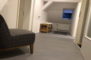 Ein Zimmer mit einem Sessel, einem kleinen Holztischchen, einer Heizung und einem Fenster mit Blick.