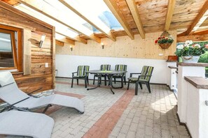 Una terrazza esterna con tetto in legno, un tavolo con sedie e un’area relax con poltrone.