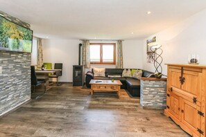 Ein Wohnzimmer mit einer Couch, einem Couchtisch und einem Kamin. Es gibt einen Essbereich mit Tisch und Stühlen sowie eine Küche mit Herd und Schränken.