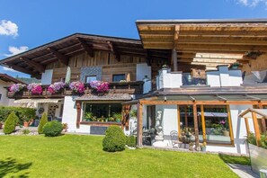 Eine zweistöckige Chalet mit Holzfassade, einem Balkon mit Blumenkästen und einem Wintergarten.