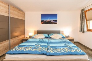 Ein Schlafzimmer mit einem Bett, Nachttischen, einem Wandbild und einem Fenster mit Vorhängen.