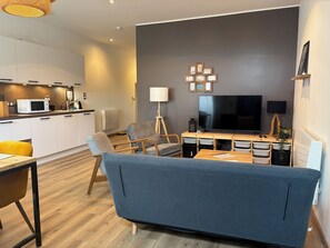 A modern living room with a sofa, a TV, and a dining area with a table and chairs.