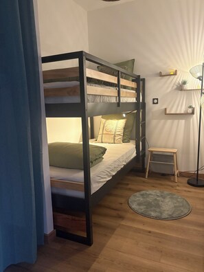 En køjeseng med træramme, et lille natbord og en gulvlampe.
