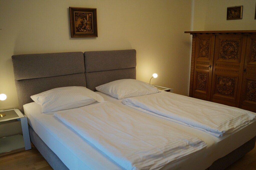 A double bed with two nightstands, each with a lamp, in a room with a wooden cabinet and a framed picture on the wall.