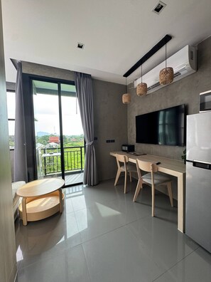 A modern kitchen with a dining area, a flat-screen TV, and a balcony with a view. - Sunrise Studio, Nai Harn, Desk, Rooftop Pool (Rawai)