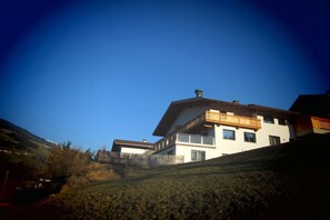 Ein modernes, zweistöckiges Haus mit Balkon, gelegen an einem Hang unter blauem Himmel.