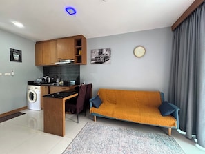 A compact living space with a kitchenette, a sofa, a rug, and a clock on the wall. - Quiet & Cozy 1br, Pool, Rawai, Walk to Gyms (Rawai)