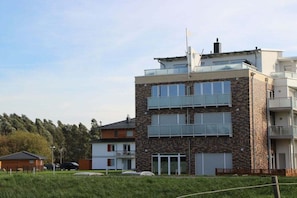 Ein mehrstöckiges Wohngebäude mit Steinaußenwand, Balkonen und einer flachen Dachterrasse.