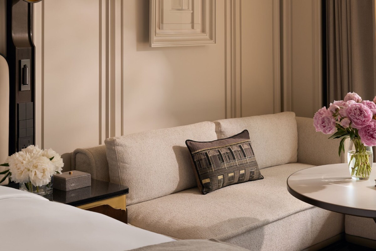 A hotel room with a sofa, a small table with a vase of flowers, and a bed.