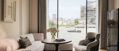 Una habitación de hotel moderna con un ventanal grande, un sofá, una silla, una mesita y una cama.