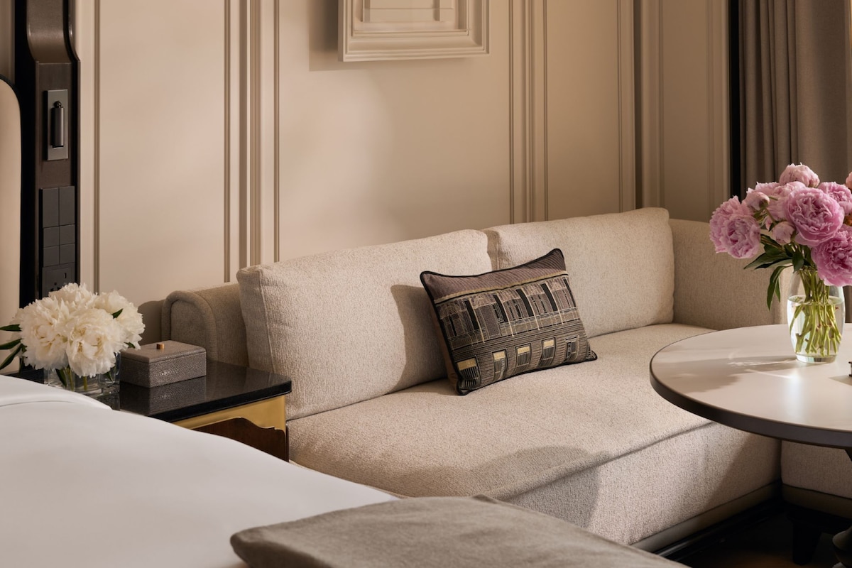 A hotel room with a sofa, a small table with a vase of flowers, and a bed.