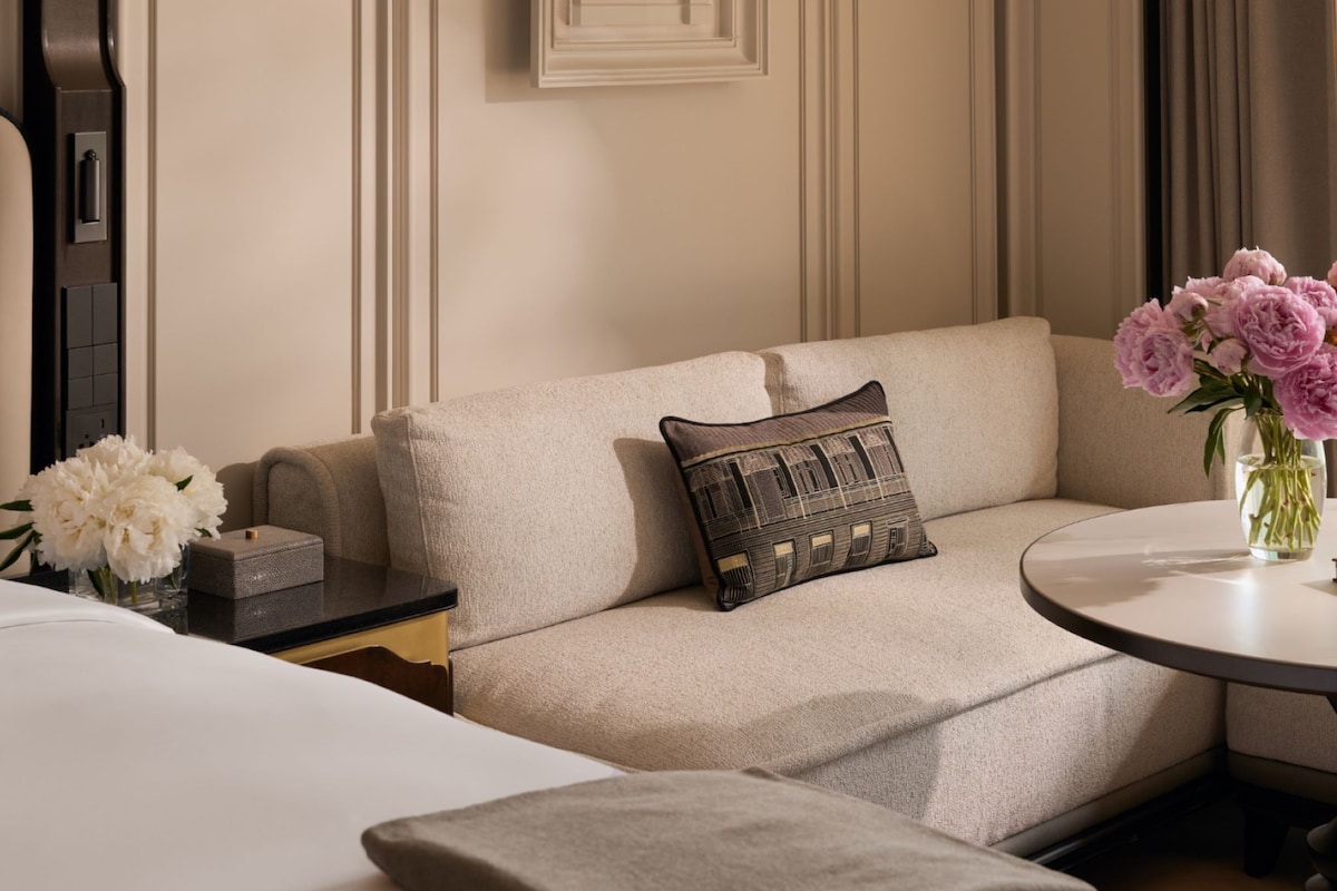 A hotel room with a bed, a sofa, a small table, and a vase with flowers.
