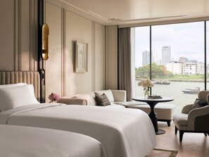 A hotel room with a large bed, a sofa, a small table, and a view of a river and cityscape. - The Langham, Custom House, Bangkok (Bangkok)