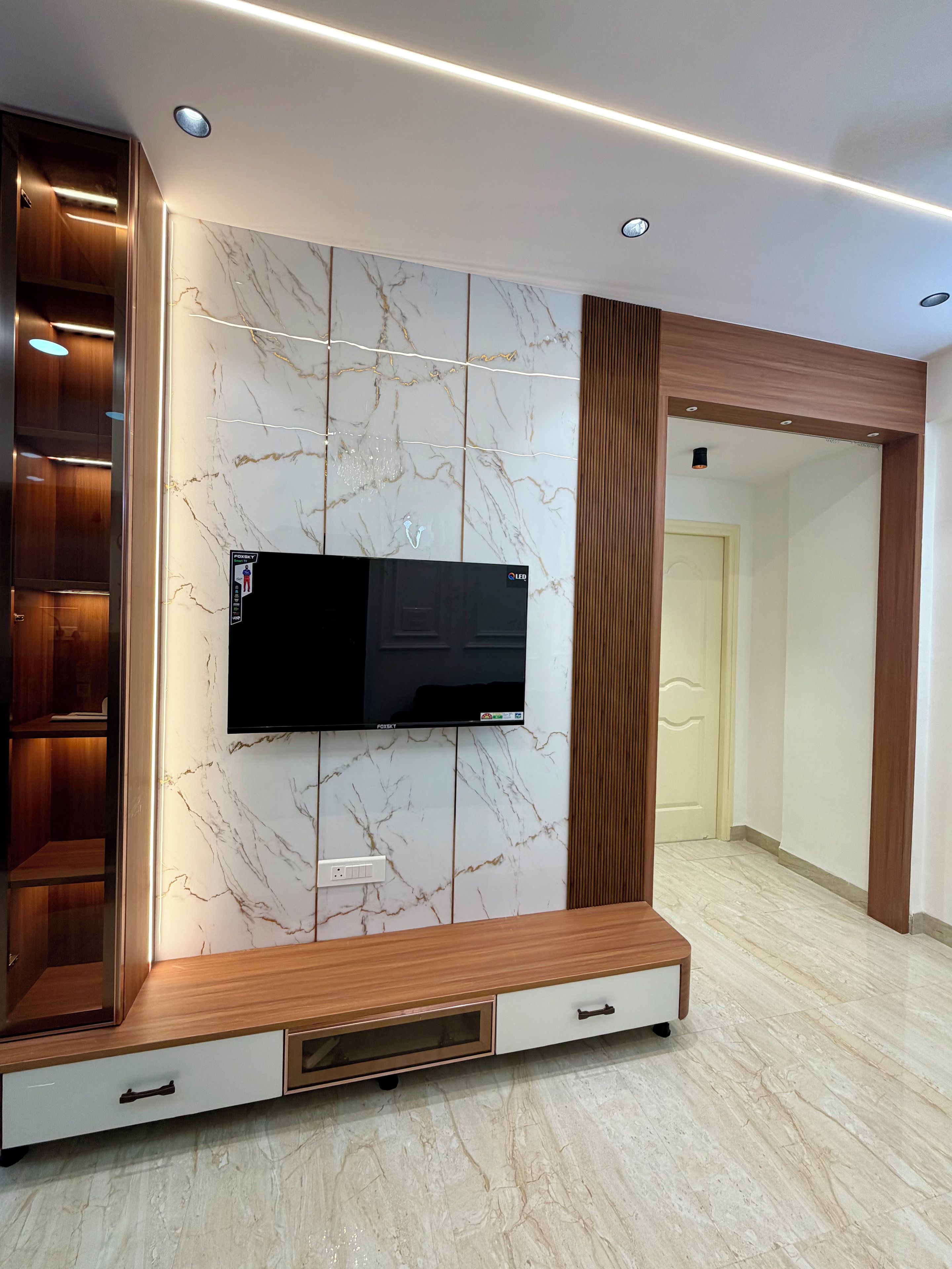 A modern entertainment unit with a flat-screen TV, wooden shelving, and marble paneling.