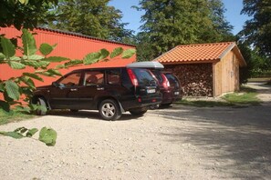 A black SUV parked on a gravel path, a red building with a tiled roof, and a stone wall. - Old cottage Beckerwitz 2 (Beckerwitz)