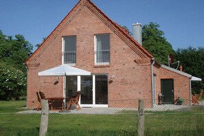 A two-story brick house with a covered patio, a sliding glass door, and a fenced yard. - Old cottage Beckerwitz 2 (Beckerwitz)