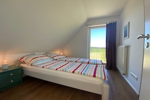 A single bed with a striped bedspread in a room with a sloped ceiling, a window with curtains, a radiator, and a green nightstand. - Old cottage Beckerwitz 2 (Beckerwitz)