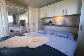 A bedroom with a bed, a wardrobe, and a shelf with decorative items. - Beach house type "Officer" (Grömitz)