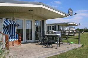 A covered outdoor area with a table and chairs, a striped beach chair, and a satellite dish. - Beach house type "Officer" (Grömitz)