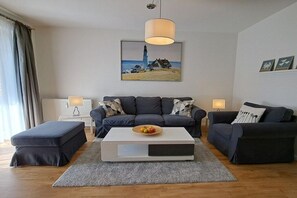 A modern living room with a sofa set, a coffee table, and a painting of a lighthouse. - Holiday apartment with 2 bedrooms (Ostseebad Boltenhagen)