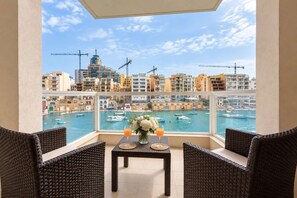 A balcony with wicker furniture, a table with drinks, and a view of a marina with boats and buildings. - Bright 2BR Flat in St. Julian's - Balcony & Views (St. Julian's)