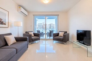 A modern living room with a sofa, two armchairs, a TV, and a glass coffee table. - Bright 2BR Flat in St. Julian's - Balcony & Views (St. Julian's)