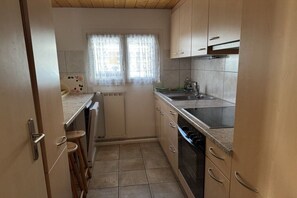Uma cozinha compacta com forno embutido, pia e janela com cortinas de renda.