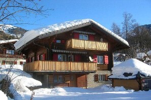A two-story wooden chalet with balconies, surrounded by snow-covered mountains.
