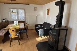 Uma sala de estar acolhedora com área de jantar, um sofá preto, uma mesa de madeira e uma lareira.