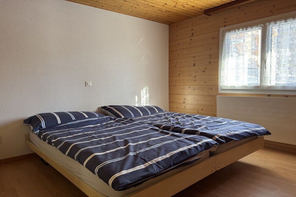 A single bed with a striped bedspread in a room with wooden walls and a window with lace curtains.