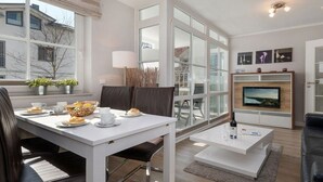 Een moderne woonkamer met een eetgedeelte, grote ramen, een flatscreen televisie en een open haard.