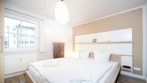 Een hotelkamer met een groot bed, een nachtkastje, een raam met gordijnen en een wandplank.